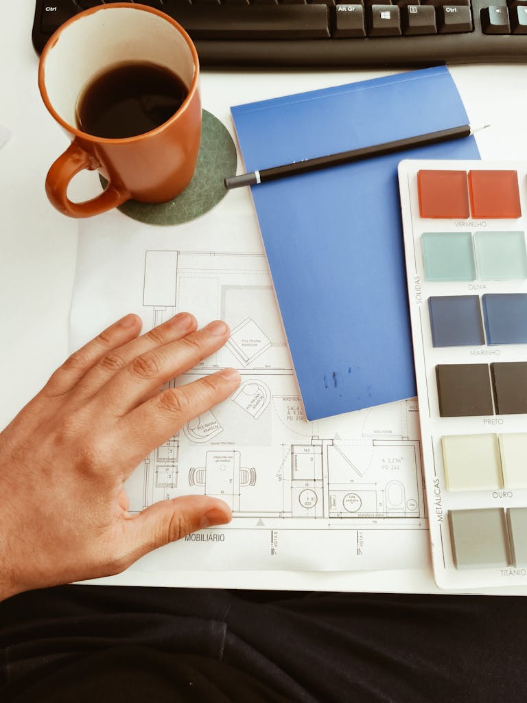 A workspace featuring a coffee cup, color palette, and architectural plans, perfect for design projects.