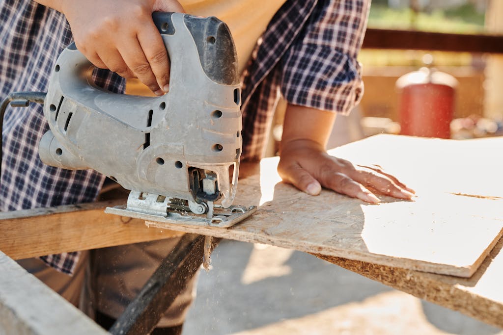 Carpenter using a jigsaw to cut plywood at a construction site, showcasing woodworking skill.
