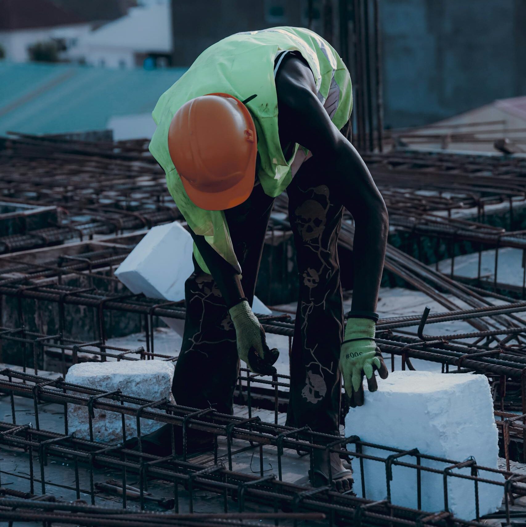 Construction worker with safety gear placing concrete block. Urban building site during the day.
