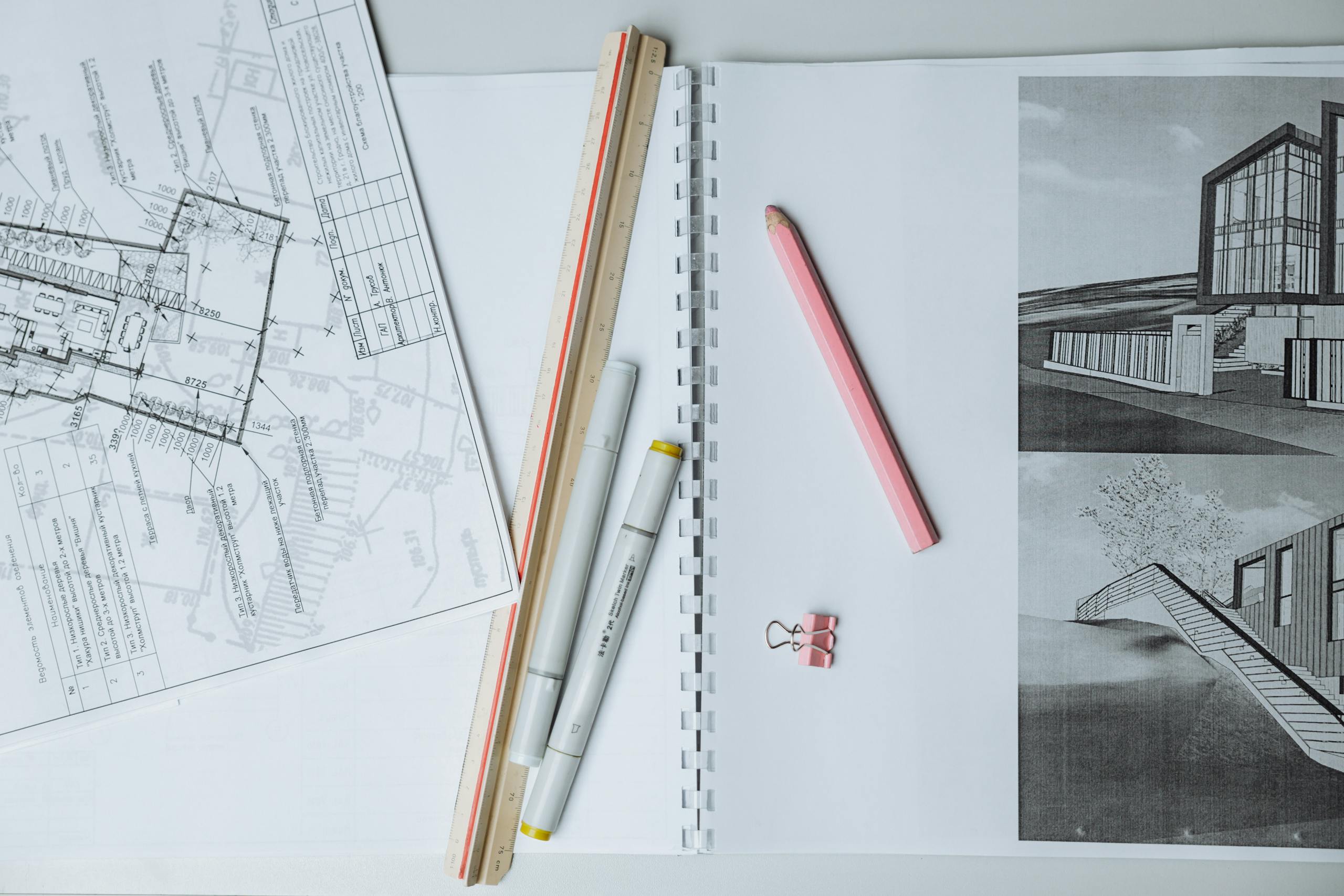 Flat lay of architectural blueprints, drawing tools, and stationery on a desk surface.