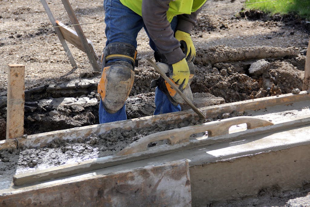 Worker using a trowel to smooth concrete at an outdoor construction site.