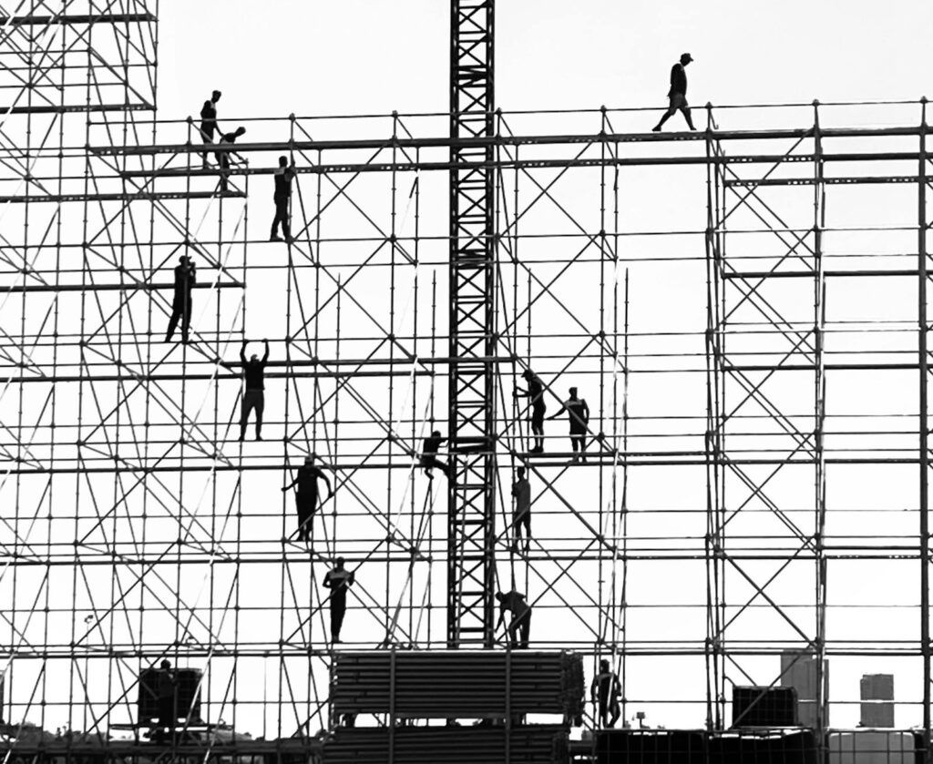 Silhouetted workers on scaffolding against the sky, depicting urban construction dynamics.