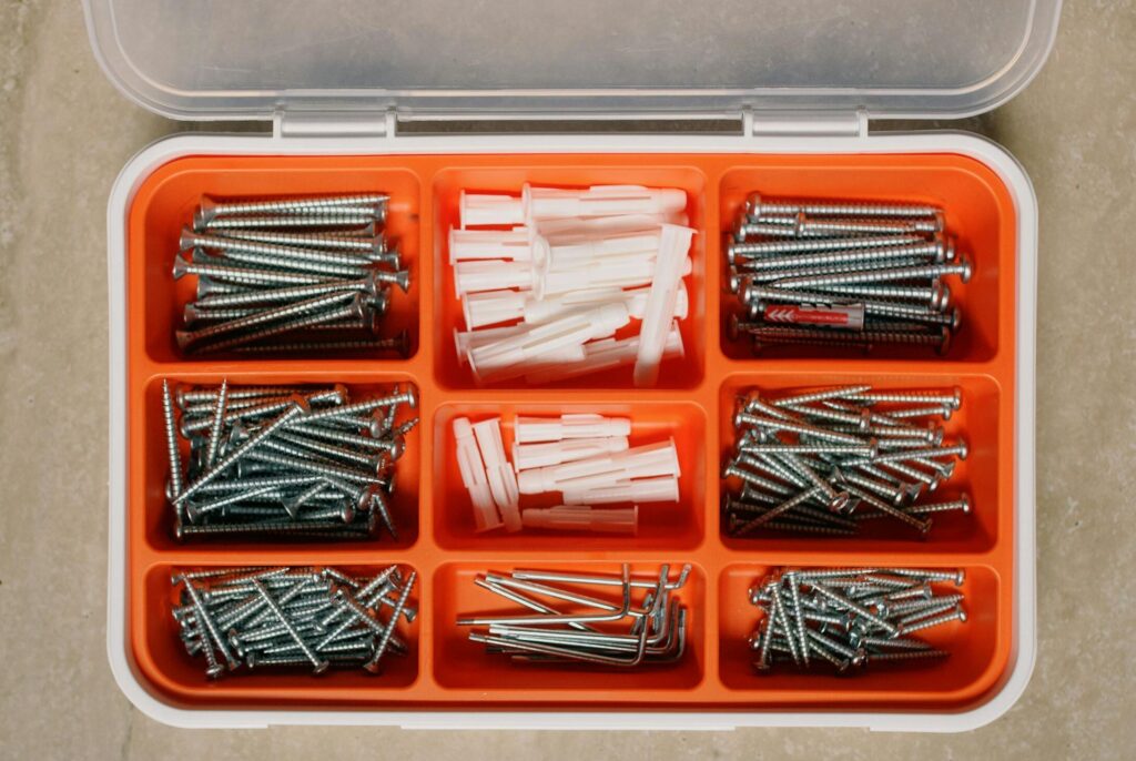 Top view of collection of different metal nails and plastic dowels in box on table