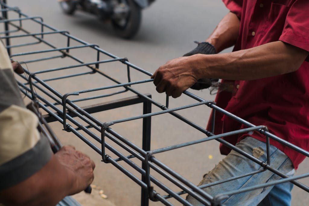 Two workers assembling a metal frame on a street, showcasing teamwork and craftsmanship in Indonesia.